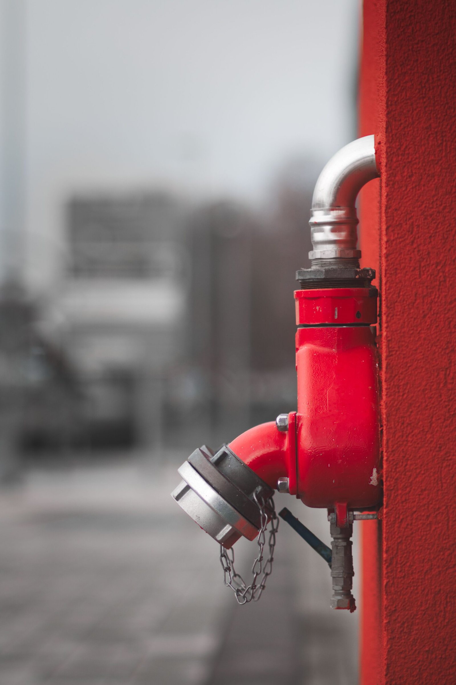Detailed view of a red fire hydrant mounted on an urban wall with blurred city background.